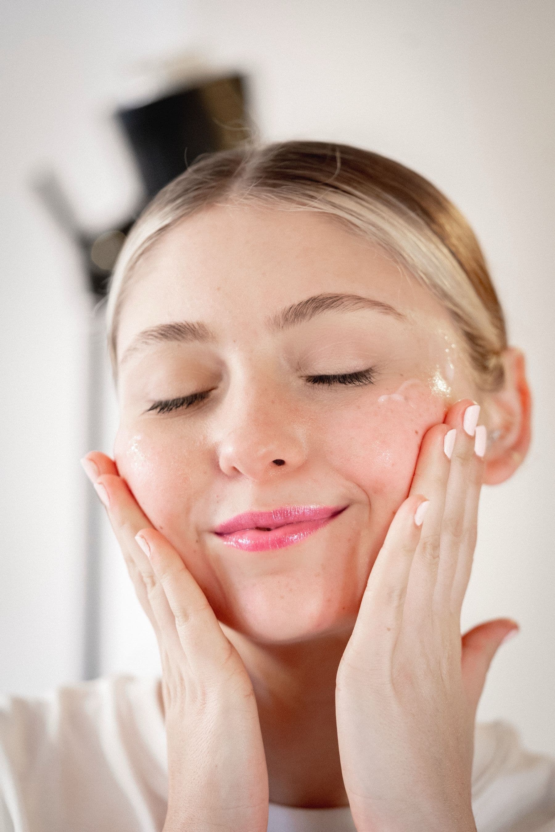 A client applying skincare, eyes closed, in soft light